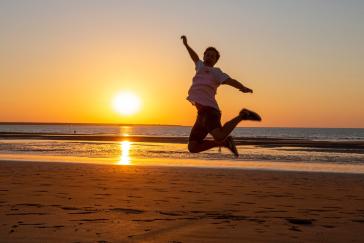 a person jumps for joy on a beach at sunset
